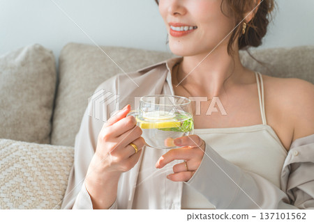 A woman sitting on a sofa drinking lemon water, detox water A woman sitting on a sofa drinking lemon water, detox water 137101562