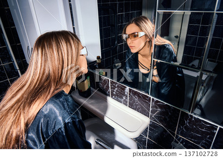 Drunken woman touching her face, looking at her reflection in a bathroom mirror 137102728