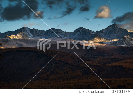 Snow-capped mountain range under cloudy sky with forested foreground at dusk Snow-capped mountain range under cloudy sky with forested foreground at dusk 137103129