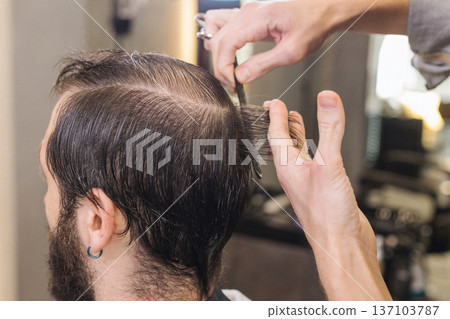 Barber cutting male client hair with scissors and comb. Close up of professional haircut process, precision technique, men grooming service in modern barbershop. Barber cutting male client hair with scissors and comb. Close up of professional haircut process, precision technique, men grooming service in modern barbershop. 137103787