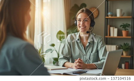 Friendly customer support representative wearing a headset, smiling during a conversation in a cozy home office with natural sunlight and plants 137104516