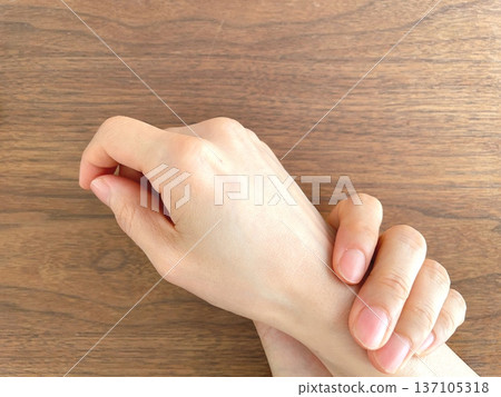 Woman's hand holding her wrist on a wooden table Woman's hand holding her wrist on a wooden table 137105318