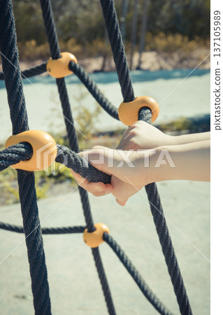 Hands of little preschooler and black rope as mesh for climbing on playground in park Hands of little preschooler and black rope as mesh for climbing on playground in park 137105989