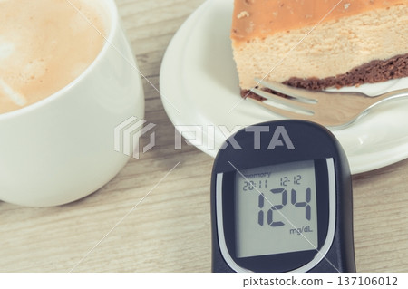Glucometer with high result sugar level, portion of sweet cheesecake and cup of coffee with milk. Glucometer with high result sugar level, portion of sweet cheesecake and cup of coffee with milk. 137106012