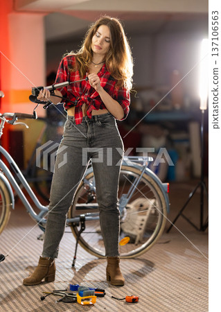 Woman repairing bicycle part with screwdriver in garage 137106563