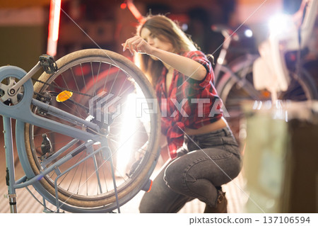 Young woman repairing bicycle chain in workshop 137106594