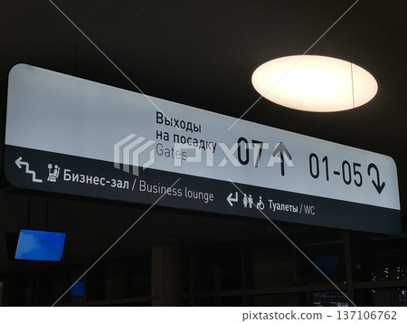 Airport directional sign showing gates and business lounge icons in russian and english for terminal wayfinding and signage design Airport directional sign showing gates and business lounge icons in russian and english for terminal wayfinding and signage design 137106762
