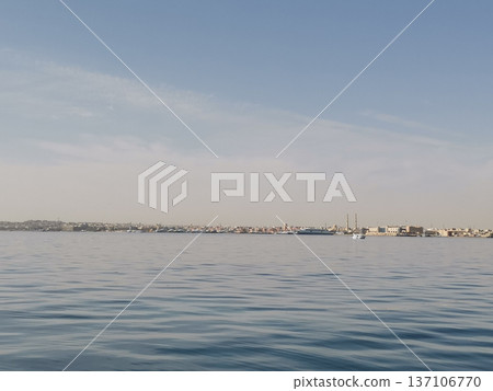 Wide tranquil bay with gentle ripples and distant coastal town skyline for calm seascape background and landscape design Wide tranquil bay with gentle ripples and distant coastal town skyline for calm seascape background and landscape design 137106770
