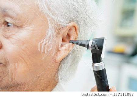 Otolaryngologist or ENT physician doctor examining senior patient ear with otoscope, hearing loss problem. 137111092