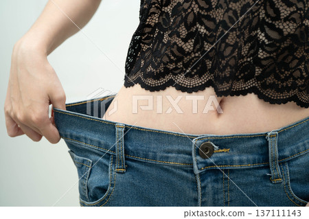 Young Asian woman losing weight wearing loose pants in oversize jeans. 137111143
