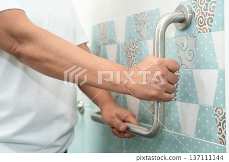 Asian woman patient use toilet support rail in bathroom, handrail safety grab bar, security in nursing hospital. 137111144