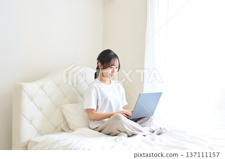 一名女子躺在床上用電腦工作。 一名女子躺在床上用電腦工作。 137111157