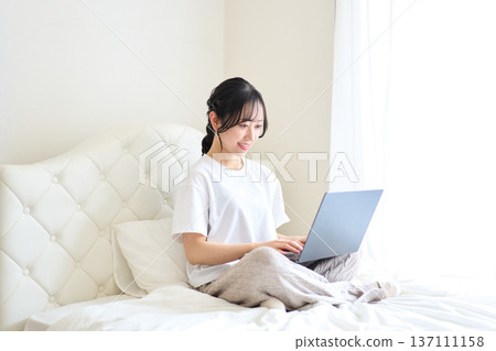 一名女子躺在床上用電腦工作。 一名女子躺在床上用電腦工作。 137111158