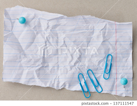 A crumpled, torn sheet of lined paper is attached with two blue pushpins to a gray background A crumpled, torn sheet of lined paper is attached with two blue pushpins to a gray background 137111547