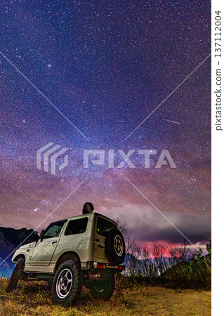An off-road vehicle under a shooting star and the Milky Way. A fantastic night view of the starry sky and earth. 137112004