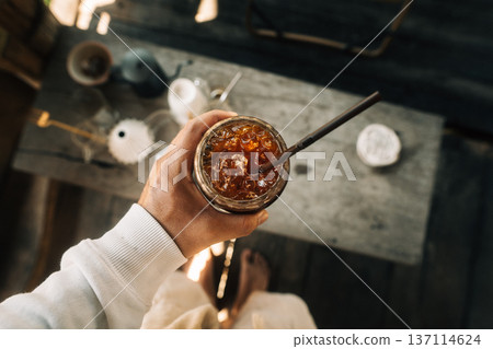 POV of a person holding a glass of iced cold brew coffee at an outdoor cafe. POV of a person holding a glass of iced cold brew coffee at an outdoor cafe. 137114624