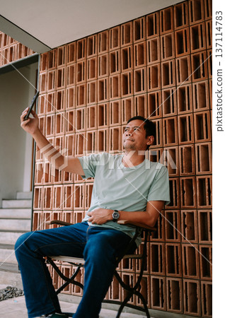Casual Man Taking a Selfie with Smartphone Against Modern Wall Casual Man Taking a Selfie with Smartphone Against Modern Wall 137114783