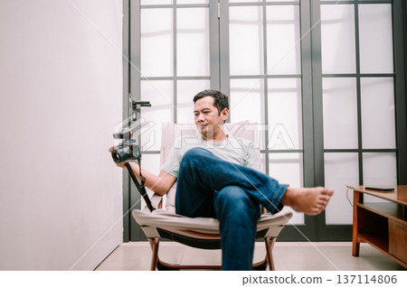 Relaxed man with camera enjoying a quiet moment at home Relaxed man with camera enjoying a quiet moment at home 137114806