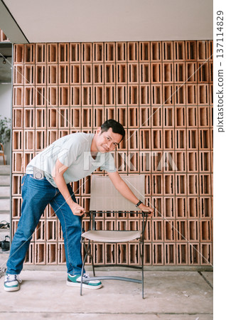 Smiling Man Posing with Chair Against Modern Terracotta Brick Wall 137114829