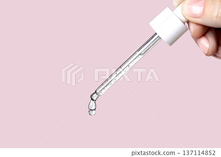 Pipette with serum in hand. Drips drop isolated on pink background, copy space photo close up 137114852