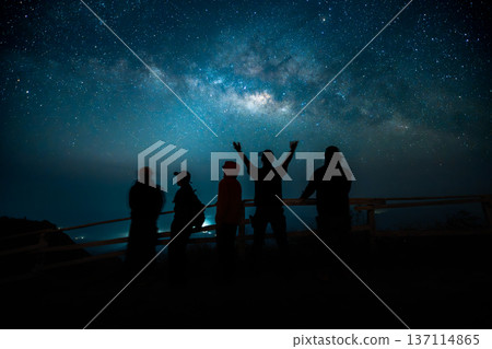 Silhouettes of hikers watching the beautiful Milky Way galaxy in the night sky from a mountain peak. Silhouettes of hikers watching the beautiful Milky Way galaxy in the night sky from a mountain peak. 137114865