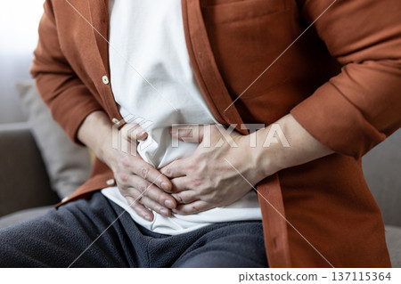 Man experiences acute stomachache, clutching his distressed abdomen with both hands, highlighting digestive issues, illness, and general discomfort associated with abdominal pain Man experiences acute stomachache, clutching his distressed abdomen with both hands, highlighting digestive issues, illness, and general discomfort associated with abdominal pain 137115364