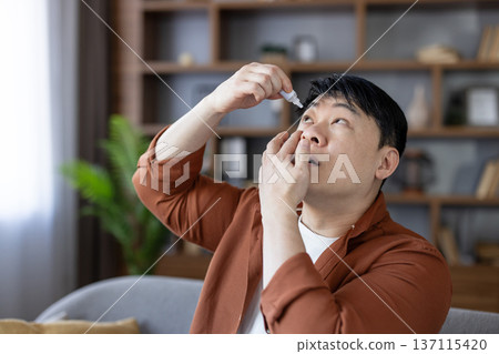 Asian man applying soothing eye drops, getting relief from dry eyes, allergies, or an eye condition, focusing on self-care and medical treatment at home Asian man applying soothing eye drops, getting relief from dry eyes, allergies, or an eye condition, focusing on self-care and medical treatment at home 137115420