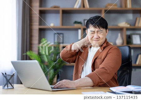 Asian man experiencing severe neck discomfort and pain, rubbing his sore neck while working from home on a laptop, highlighting occupational health issues and poor posture Asian man experiencing severe neck discomfort and pain, rubbing his sore neck while working from home on a laptop, highlighting occupational health issues and poor posture 137115435