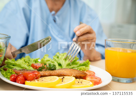 Asian elderly woman patient eating salmon stake and vegetable salad for healthy food in hospital. Asian elderly woman patient eating salmon stake and vegetable salad for healthy food in hospital. 137115535