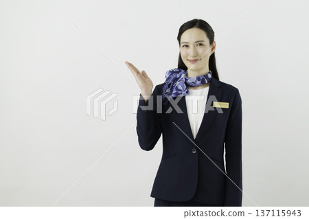 A smiling Japanese woman concierge wearing a navy suit, ribbon, and name tag holding her hand up against a white background A smiling Japanese woman concierge wearing a navy suit, ribbon, and name tag holding her hand up against a white background 137115943