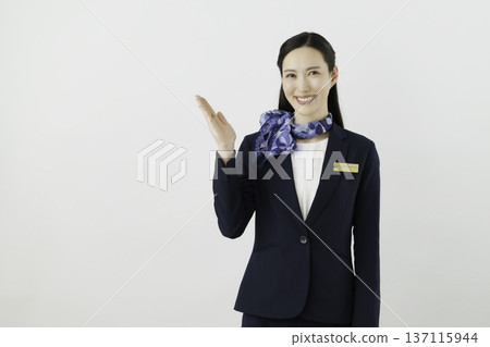 A smiling Japanese woman concierge wearing a navy suit, ribbon, and name tag holding her hand up against a white background A smiling Japanese woman concierge wearing a navy suit, ribbon, and name tag holding her hand up against a white background 137115944