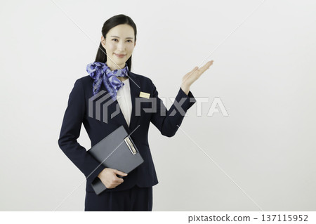 A smiling Japanese woman concierge wearing a navy suit, ribbon, and name tag holding her hand up against a white background A smiling Japanese woman concierge wearing a navy suit, ribbon, and name tag holding her hand up against a white background 137115952