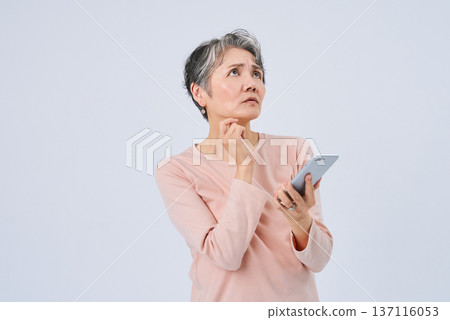 一位神情憂慮的老婦人拿著一部智慧型手機 一位神情憂慮的老婦人拿著一部智慧型手機 137116053