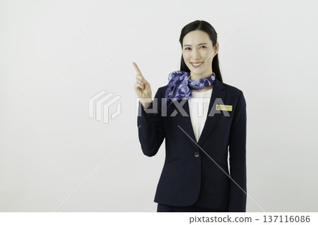 一位面帶微笑的日本女門房，身穿藏藍色套裝，佩戴絲帶和名牌，在白色背景下擺出“1號”的姿勢。 137116086