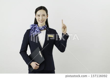 一位面帶微笑的日本女門房,身穿藏藍色套裝,佩戴絲帶和名牌,在白色背景下擺出“1號”的姿勢。 一位面帶微笑的日本女門房,身穿藏藍色套裝,佩戴絲帶和名牌,在白色背景下擺出“1號”的姿勢。 137116092