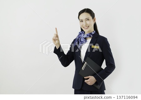 一位面帶微笑的日本女門房，身穿藏藍色套裝，佩戴絲帶和名牌，在白色背景下擺出“1號”的姿勢。 137116094