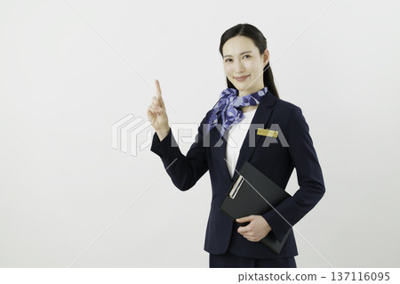 一位面帶微笑的日本女門房，身穿藏藍色套裝，佩戴絲帶和名牌，在白色背景下擺出“1號”的姿勢。 137116095