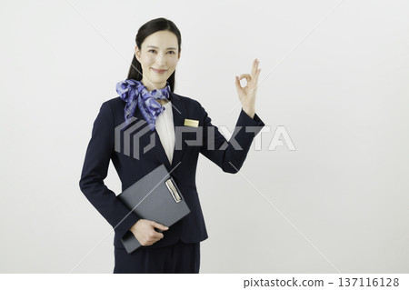 一位面帶微笑的日本女性,身穿藏藍色套裝,佩戴絲帶和名牌,站在白色背景前,手指比出一個“OK”的手勢。禮賓部 一位面帶微笑的日本女性,身穿藏藍色套裝,佩戴絲帶和名牌,站在白色背景前,手指比出一個“OK”的手勢。禮賓部 137116128
