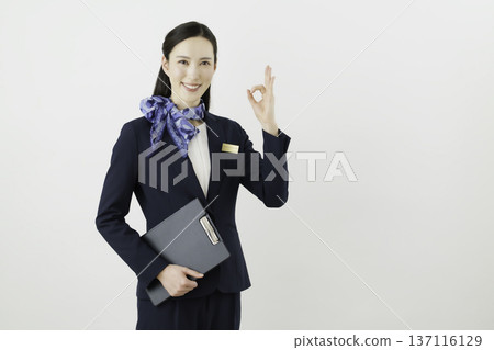 一位面帶微笑的日本女性,身穿藏藍色套裝,佩戴絲帶和名牌,站在白色背景前,手指比出一個“OK”的手勢。禮賓部 一位面帶微笑的日本女性,身穿藏藍色套裝,佩戴絲帶和名牌,站在白色背景前,手指比出一個“OK”的手勢。禮賓部 137116129