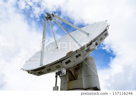 A huge white parabolic antenna towering into the clear blue sky A huge white parabolic antenna towering into the clear blue sky 137116246