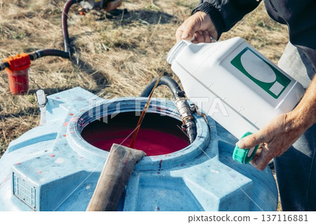 men's hands pouring a chemical into a large blue plastic tank filled, agricultural mixing process, hoses connected for chemical transfer in sunny rural field, agriculture, irrigation, chemistry men's hands pouring a chemical into a large blue plastic tank filled, agricultural mixing process, hoses connected for chemical transfer in sunny rural field, agriculture, irrigation, chemistry 137116881