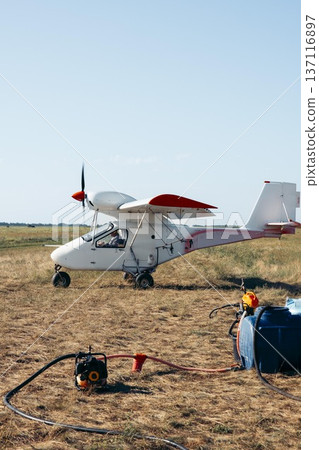 Small agricultural airplane on a farm field. The aircraft is equipped for spraying chemicals. Nearby equipment includes a tank and hoses. Small agricultural airplane on a farm field. The aircraft is equipped for spraying chemicals. Nearby equipment includes a tank and hoses. 137116897