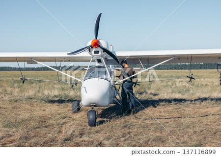 man in protective mask refueling small white aircraft on grassy airfield, aviation worker in green uniform, sunset, rural field, aviation service, pilot training, countryside tourism 137116899