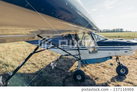 Agricultural airplane parked on a farm. The aircraft is equipped for spraying chemicals over fields. Clear sky and grassy terrain are visible. 137116908