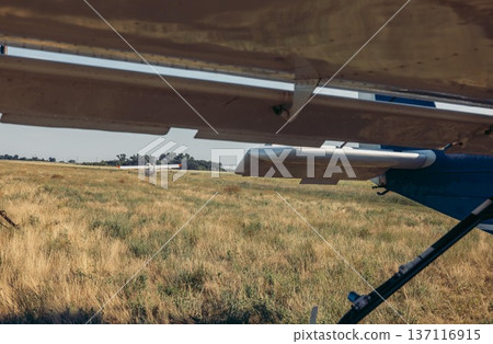 An agricultural airplane prepares for chemical spraying over a golden field. The scene captures the aircraft's wing and the vast landscape below. 137116915