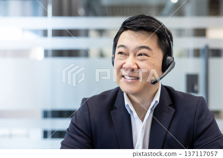 Smiling man wearing a professional headset with microphone providing excellent customer assistance and communication services, looking away with a friendly expression in a modern office environment Smiling man wearing a professional headset with microphone providing excellent customer assistance and communication services, looking away with a friendly expression in a modern office environment 137117057