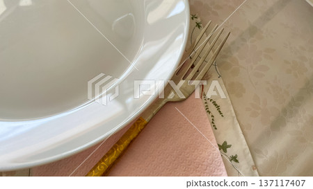 Elegant table setting with white porcelain plate and golden fork on a pink napkin for celebration. 137117407