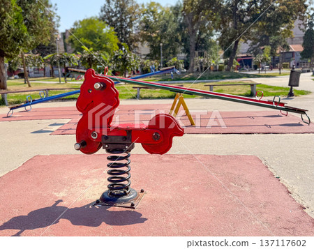 Red spring rider on the playground. Fun, balance and childhood activity in an outdoor park. 137117602