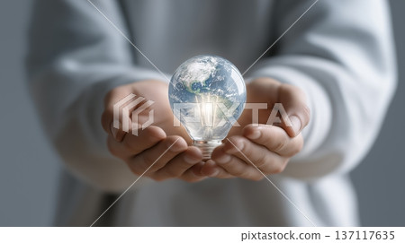 Hands hold a light bulb with a view of Earth inside, symbolizing sustainability and energy 137117635