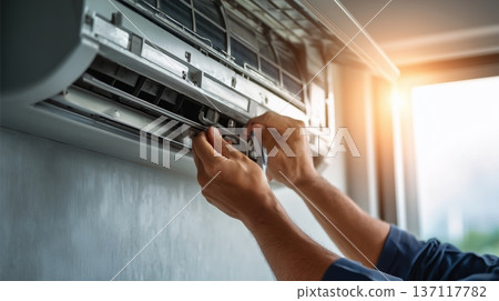 Worker repairs an air conditioning unit in a building during daylight hours with sunlight filtering through the window 137117782